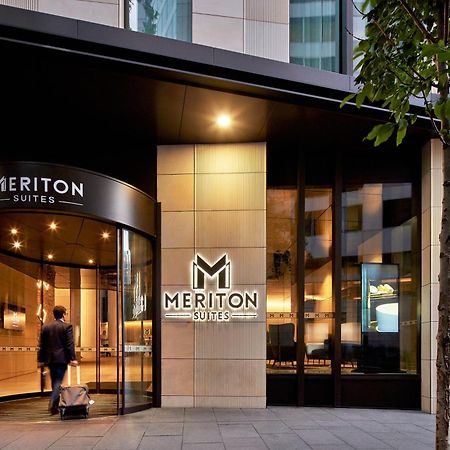 Meriton Suites Sussex Street, Sydney Exterior photo The photo shows the entrance of a hotel or suite establishment named "Meriton Suites." The entrance features a revolving door and a large, illuminated sign with the name "MERITON SUITES." The facade is modern and sleek, with a combination of glass an