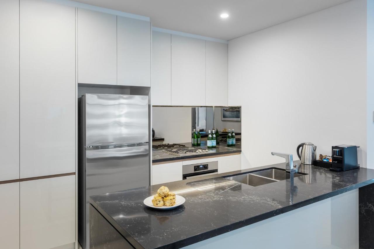 Meriton Suites Sussex Street, Sydney Exterior photo The photo shows a modern kitchen with a sleek, minimalist design. Key features include:

- A shiny stainless steel refrigerator on the left.
- A mirrored backsplash above the stove, which has a gas burner.
- A dark countertop made of what appears to 