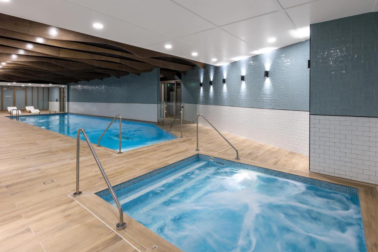 Meriton Suites Sussex Street, Sydney Exterior photo The photo shows a modern indoor spa area. There are two pools: one is larger and has a clear blue water, while the other is smaller, possibly a hot tub, with jets creating bubbles. The walls are a mix of blue tiles and white tiles, and the floor is m