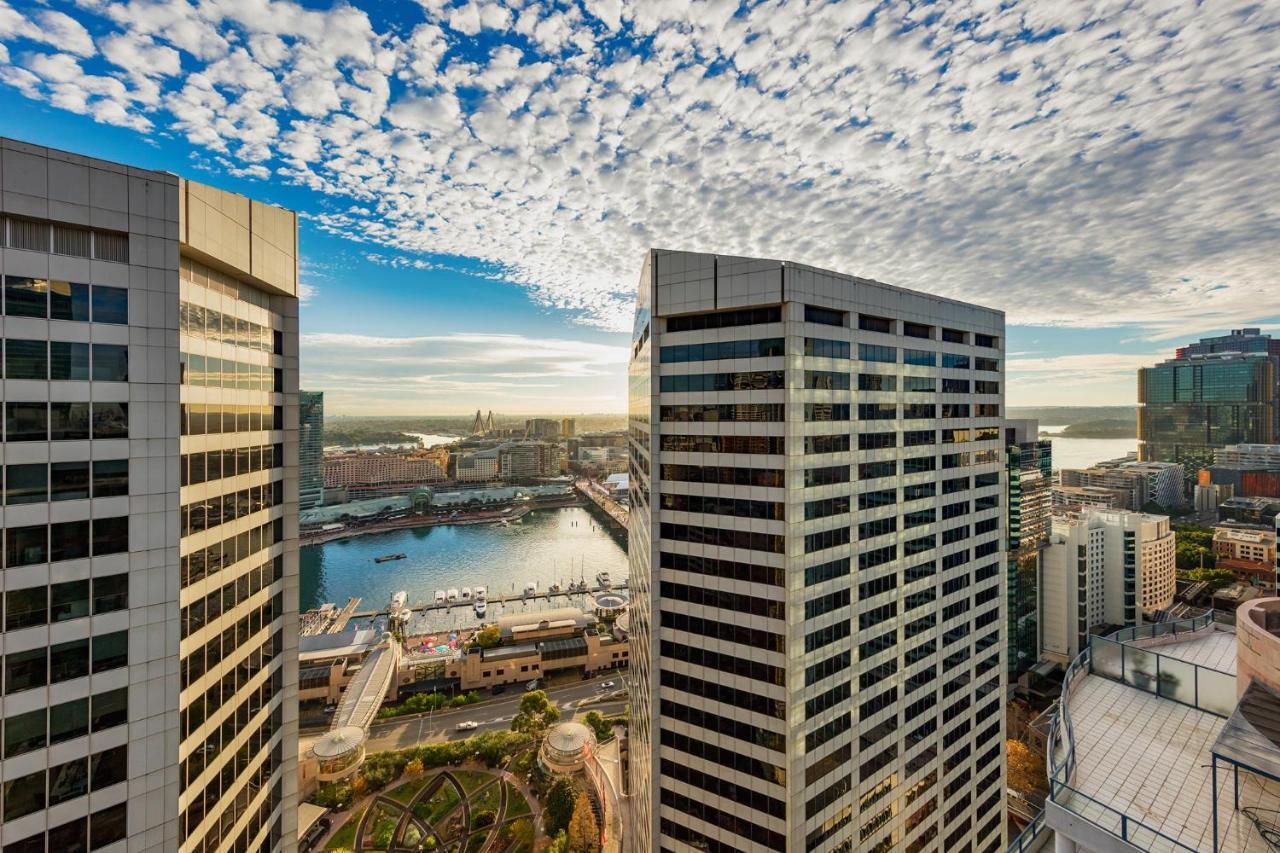 Meriton Suites Sussex Street, Sydney Exterior photo The photo depicts a panoramic view of a modern cityscape featuring tall commercial buildings with glass facades. The shot is taken from a height, showing the intricate architecture of the nearby structures. Below, there is a body of water, which appe