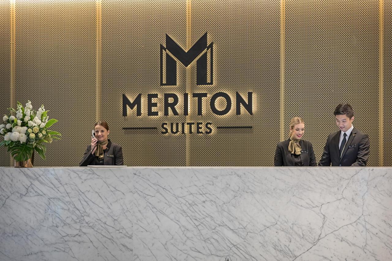 Meriton Suites Sussex Street, Sydney Exterior photo The photo depicts the reception area of a hotel called "Meriton Suites." In the background, there is a large, illuminated sign featuring the hotel’s logo. The reception desk is made of marble and is staffed by two individuals dressed in professional 