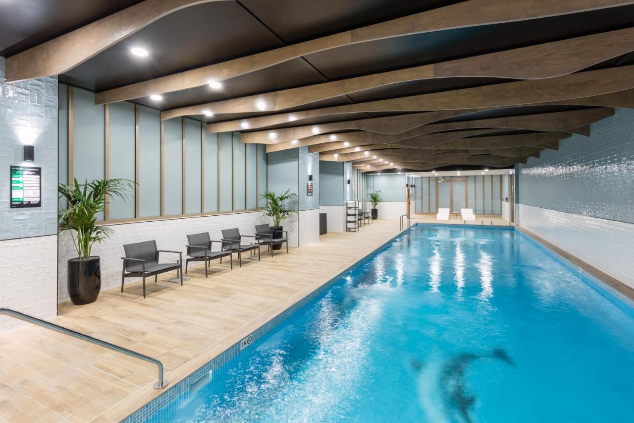 Meriton Suites Sussex Street, Sydney Exterior photo The photo shows an indoor swimming pool area. The pool has clear blue water and is flanked by a wooden deck. There are several lounge chairs arranged along one side of the pool. The ceiling features a modern design with wooden beams and recessed ligh