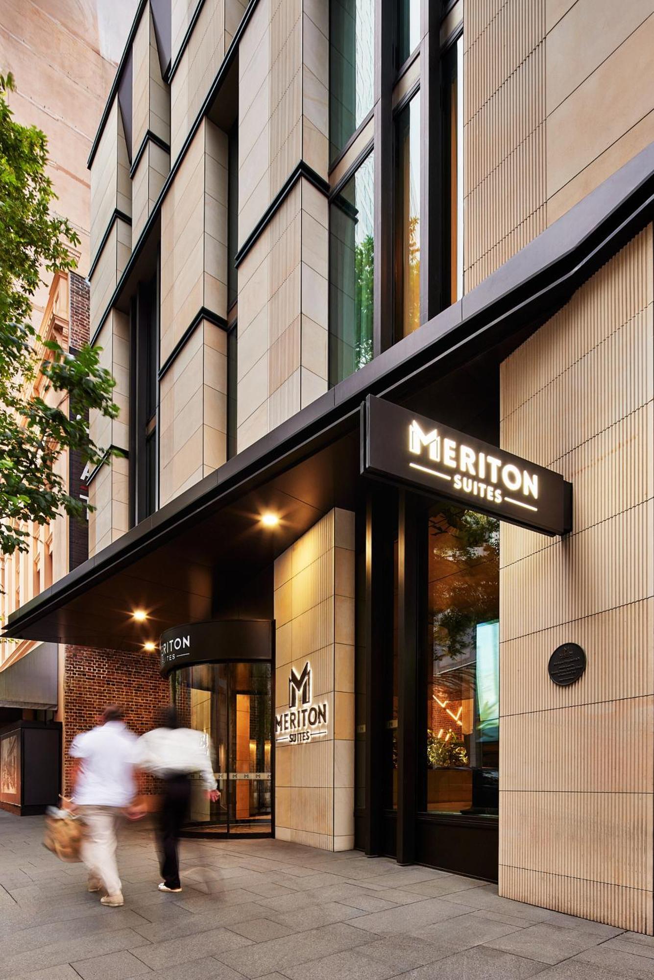 Meriton Suites Sussex Street, Sydney Exterior photo The photo shows the exterior of a building with the signage for "Meriton Suites." The entrance features a modern design, with sleek architectural elements and large windows. The entrance is highlighted by a prominent awning and illuminated signs, ind