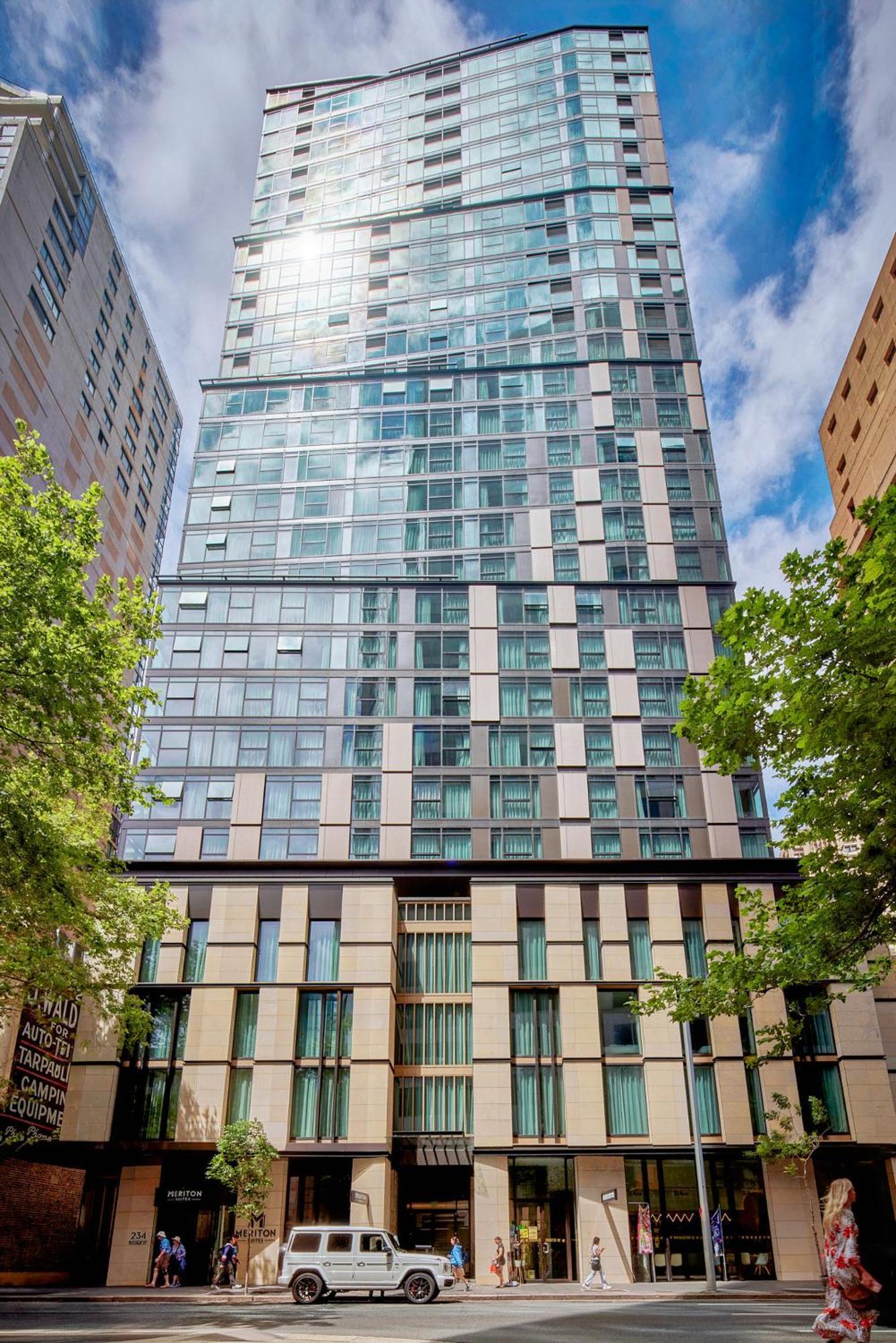 Meriton Suites Sussex Street, Sydney Exterior photo The photo shows a tall modern building with a glass facade and various architectural design elements. The structure has multiple stories, with large windows that reflect the surrounding environment. At the base, there are sections that appear to have